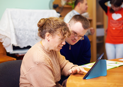 Two people sitting at a table looking at a tablet device