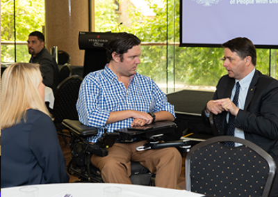 Commissioner Alastair McEwin talking with a man in a wheelchair at a community forum