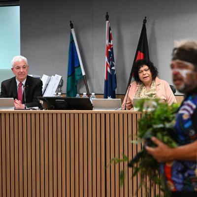Two commissioners at public hearing 31 sitting at bench watching first nations ceremony